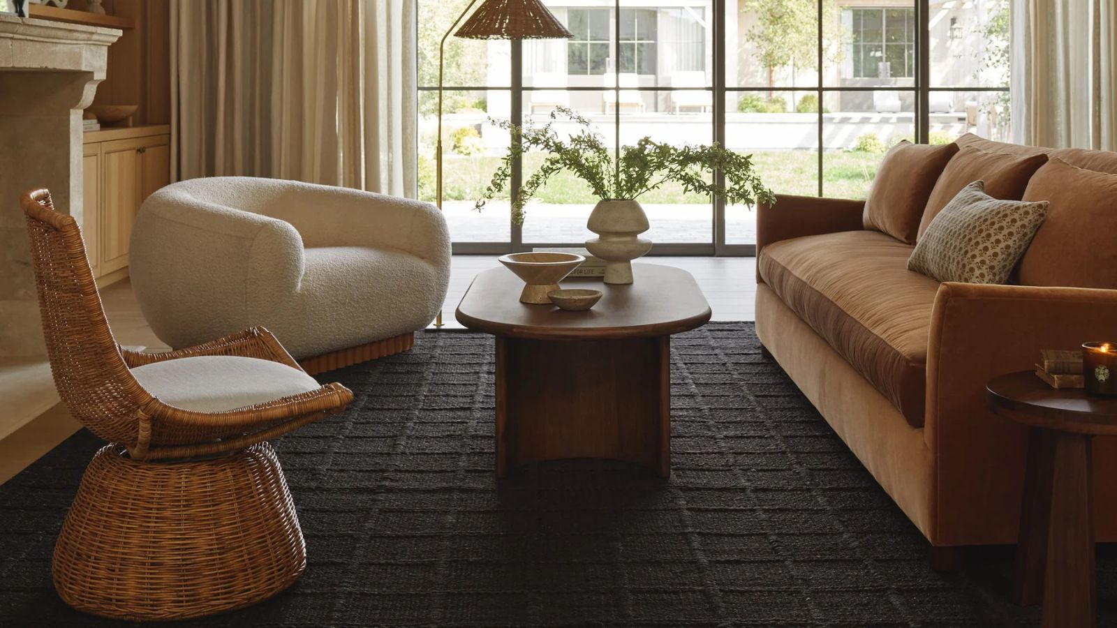 Living room with large windows, a dark rug, orange couch, cream armchair and rattan chair 