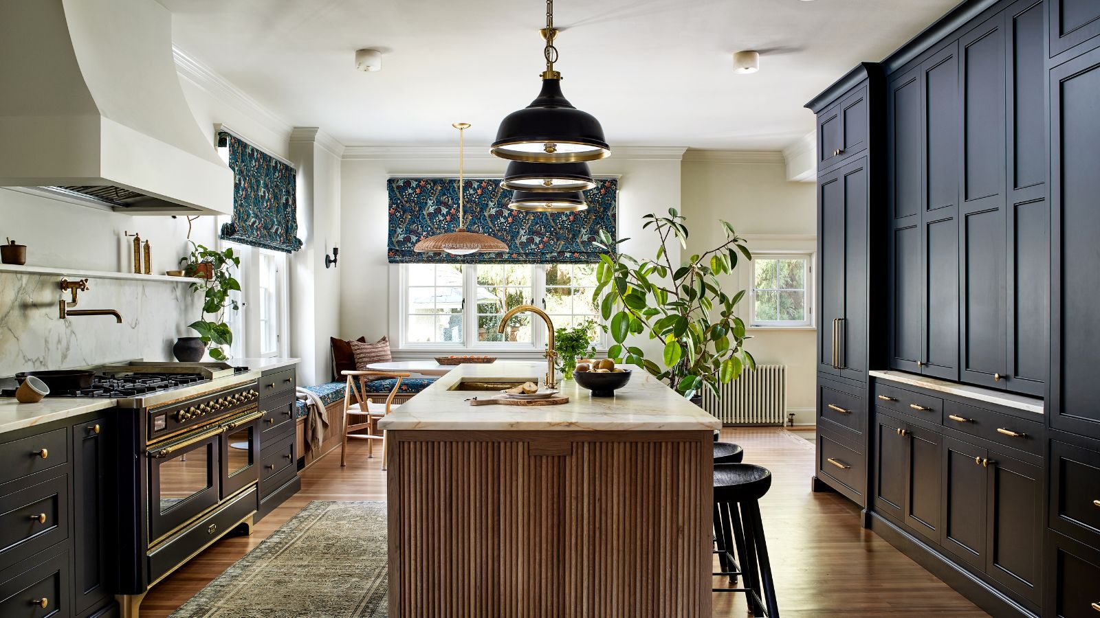 A kitchen with dark blue cabinets, white walls, a wooden island, and a dining nook with banquette seating