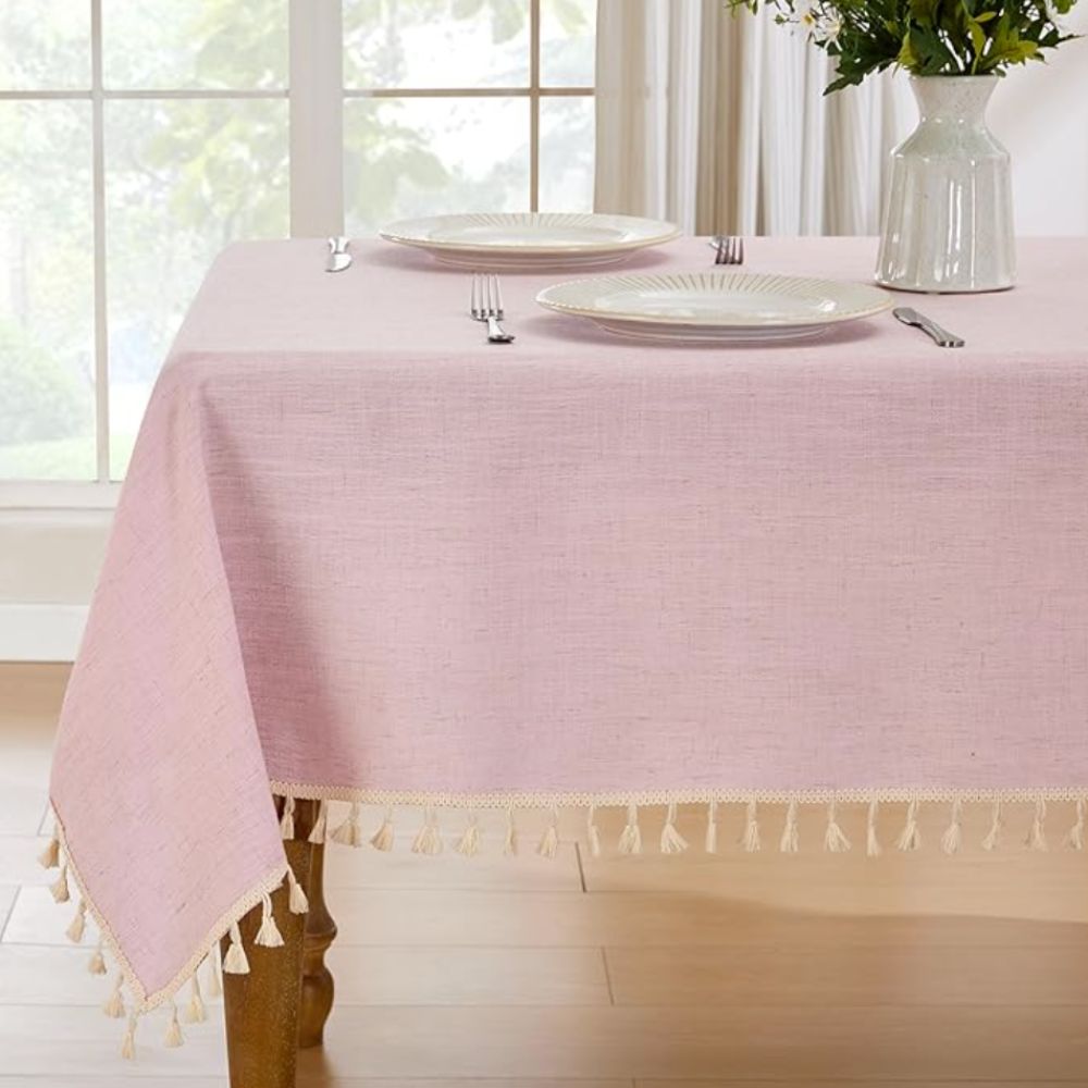 pink tablecloth with tassled on a wooden table laid with white plates and cutlery