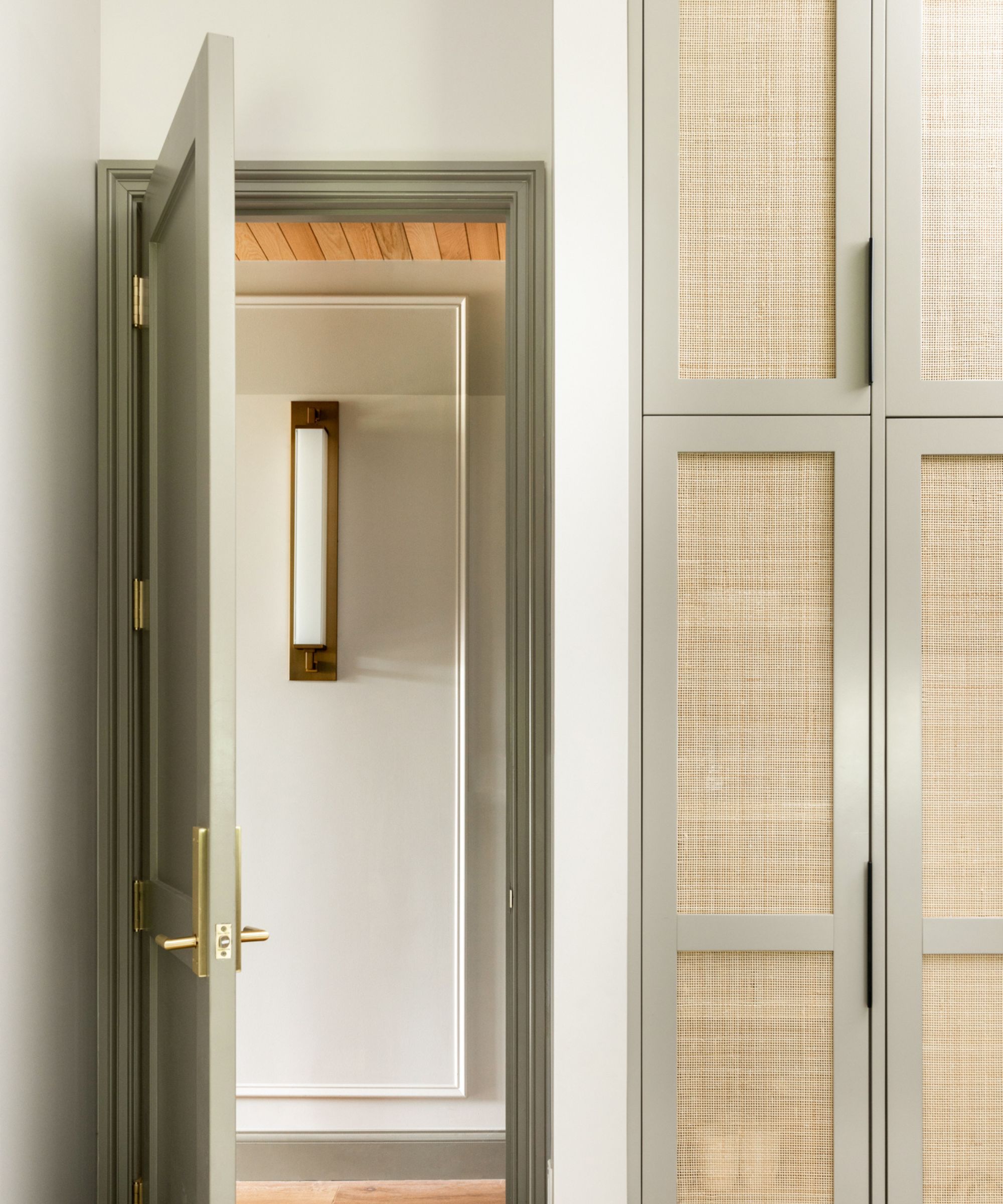 A door leading from one room to another, the walls are painted in Modern Gray by Sherwin Williams, there are large brass lighting fixed to the walls.