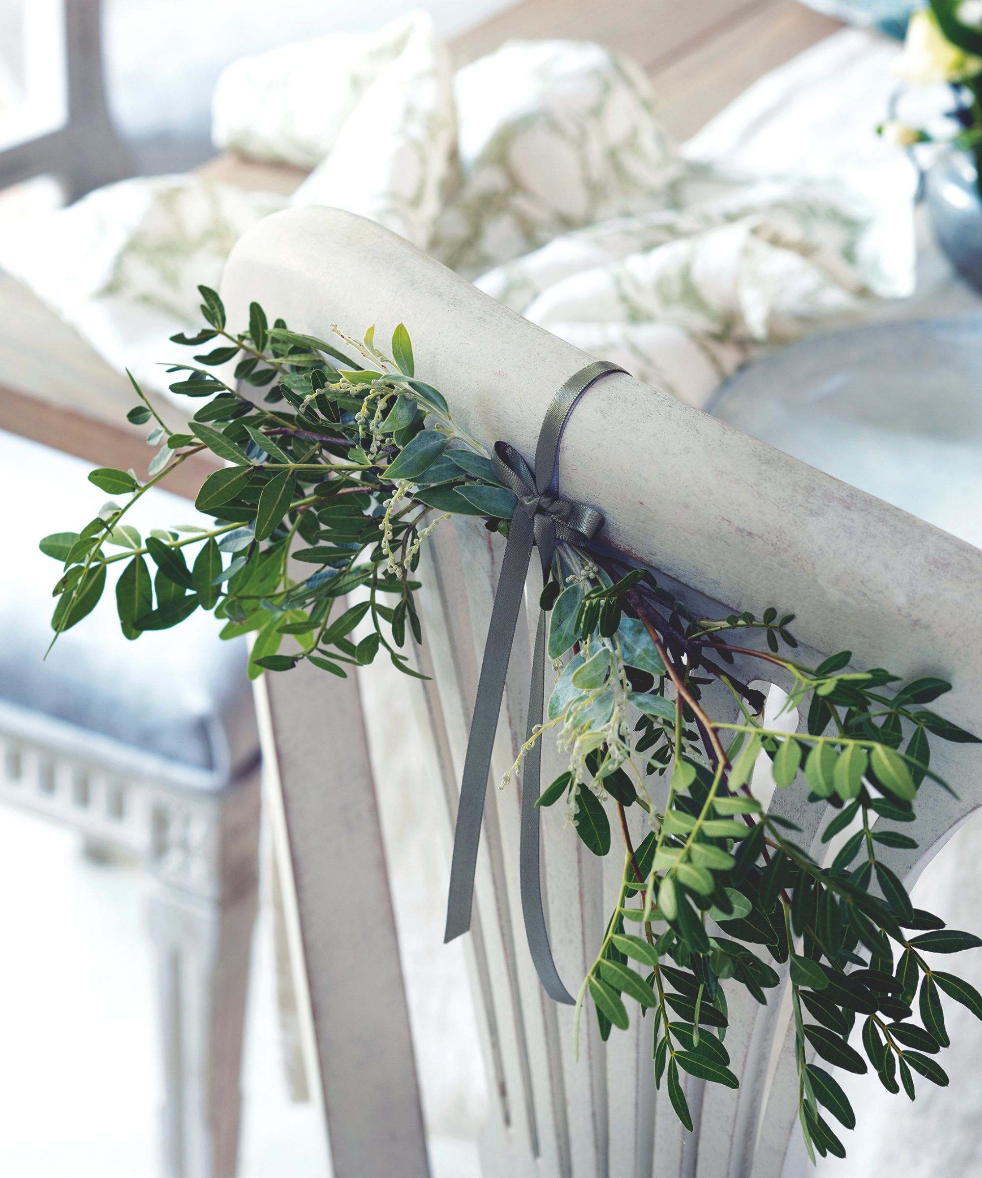 greenery tied to the back of a white dining chair with a grey ribbon