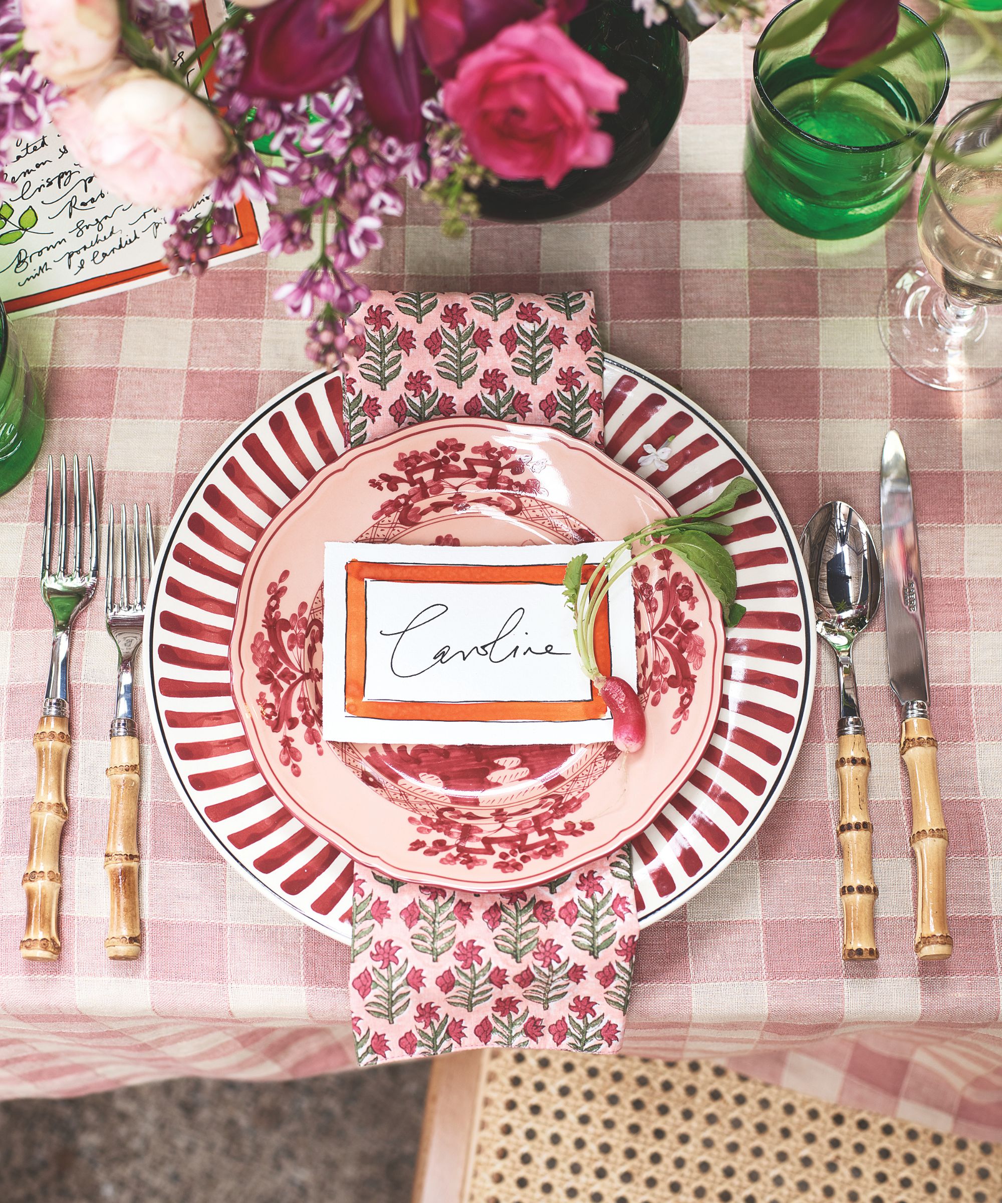 red and white place setting with gingham tablecloth, striped plate and floral napkin with a place carf and bamboo cutlery