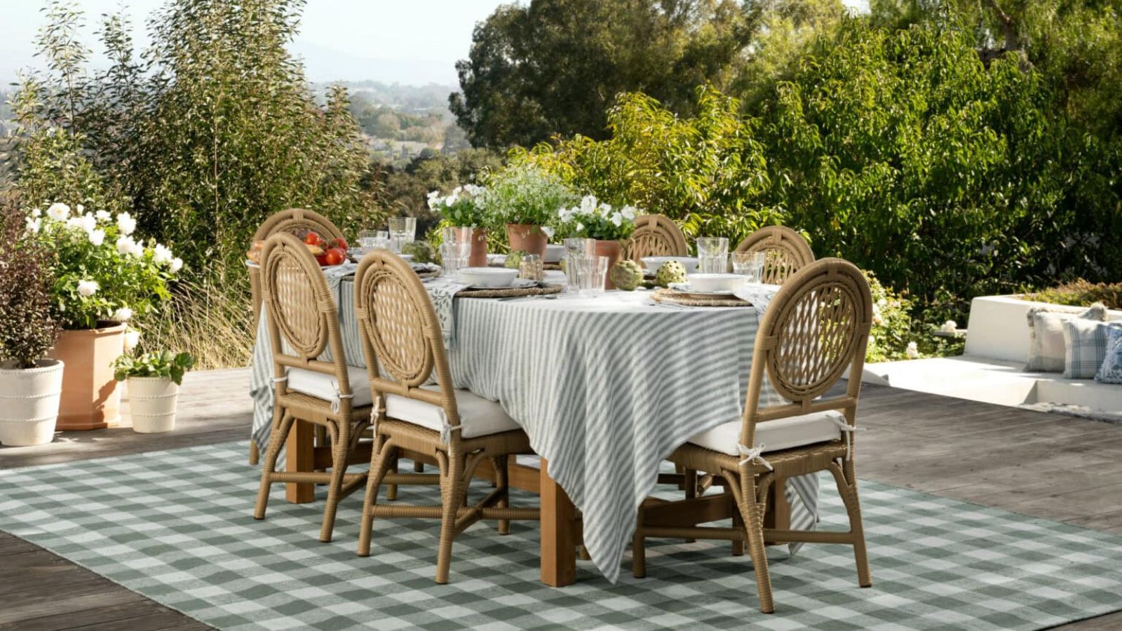 outdoor patio with a large checked rug and a rattan wicker dining table seating 6 surrounded by pots of flowers