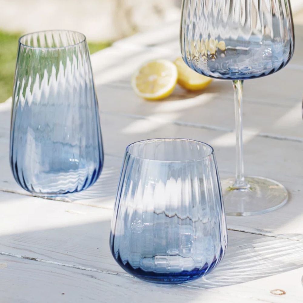 three blue glasses on a white wooden table with cut lemons in the background