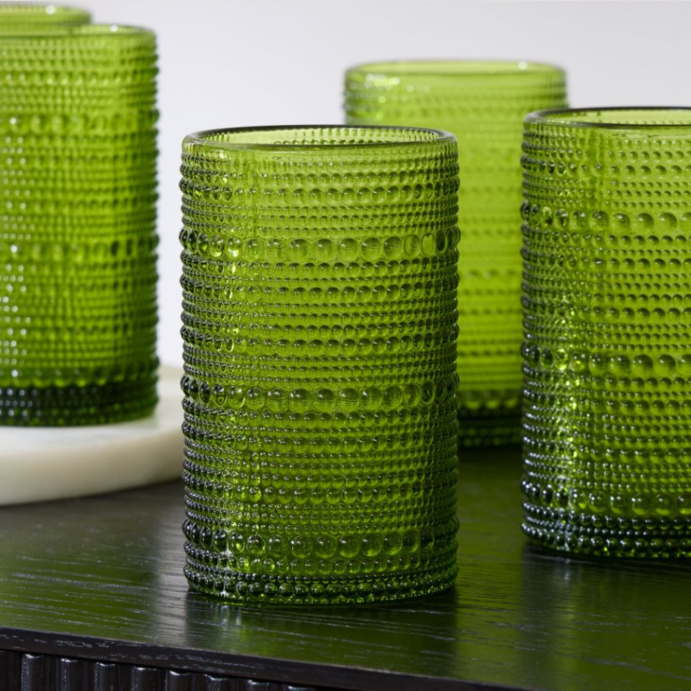Collection of green beaded hi-ball drinking glassed from West Elm on a dark wooden surface