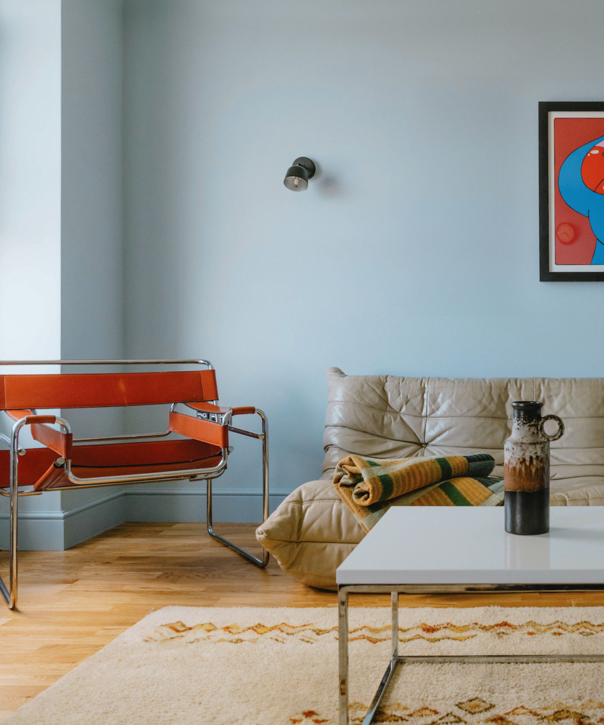 Blue living room with tapestry rug, orange midcentury metal chair and togo armchair