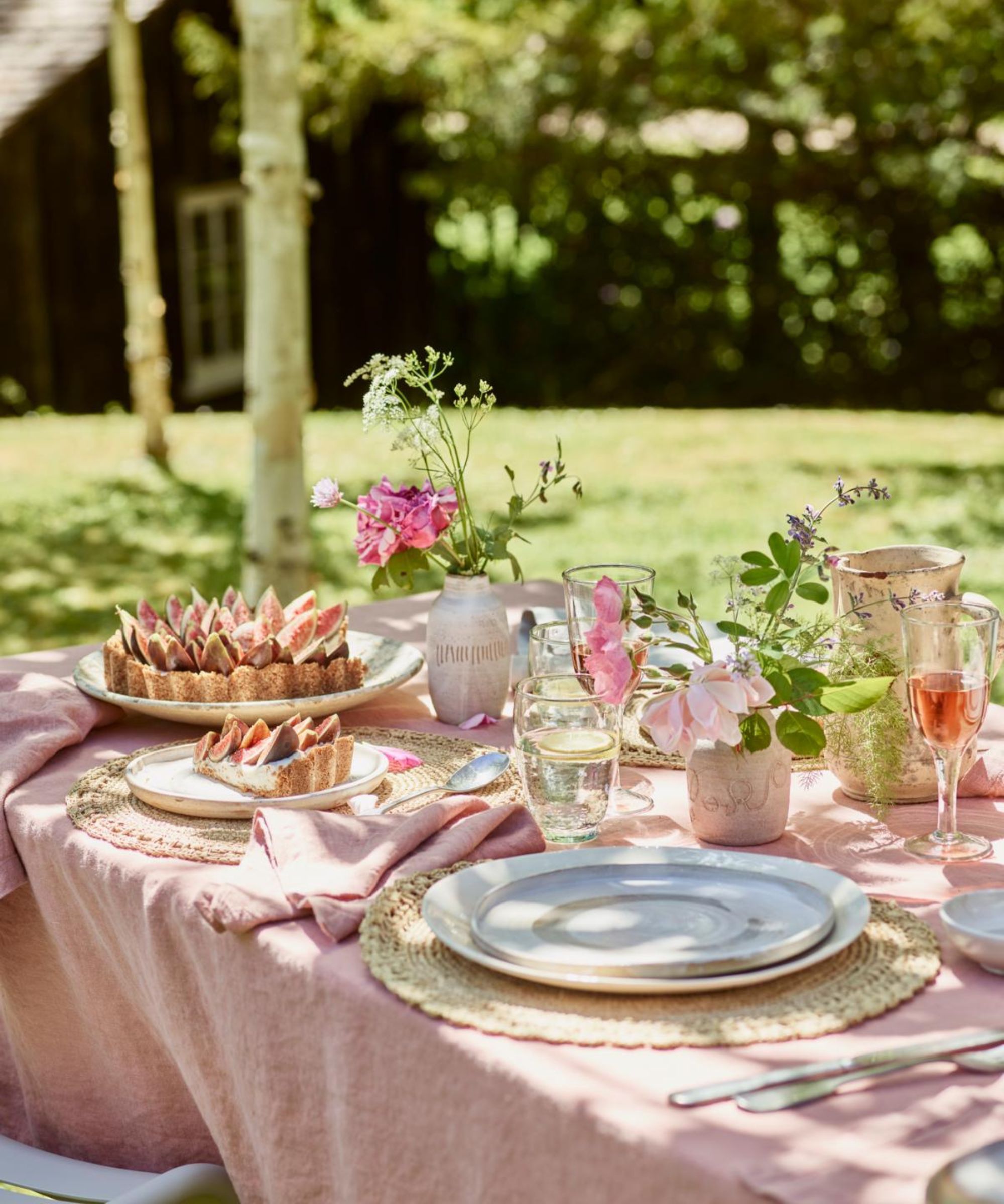 table outdoors with soft pink linen, plates and glasses of rose wine, and a fig tart