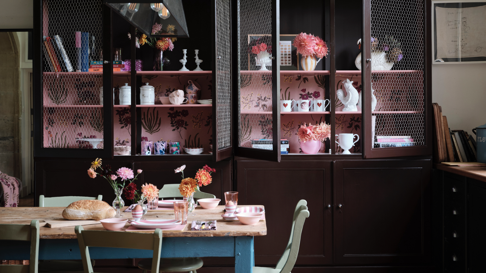 dining room kitchen with large custom cabinets with wallpaper interior/shelving, kitchen table with mint green painted chairs, flowers, vases, Farrow & Ball 