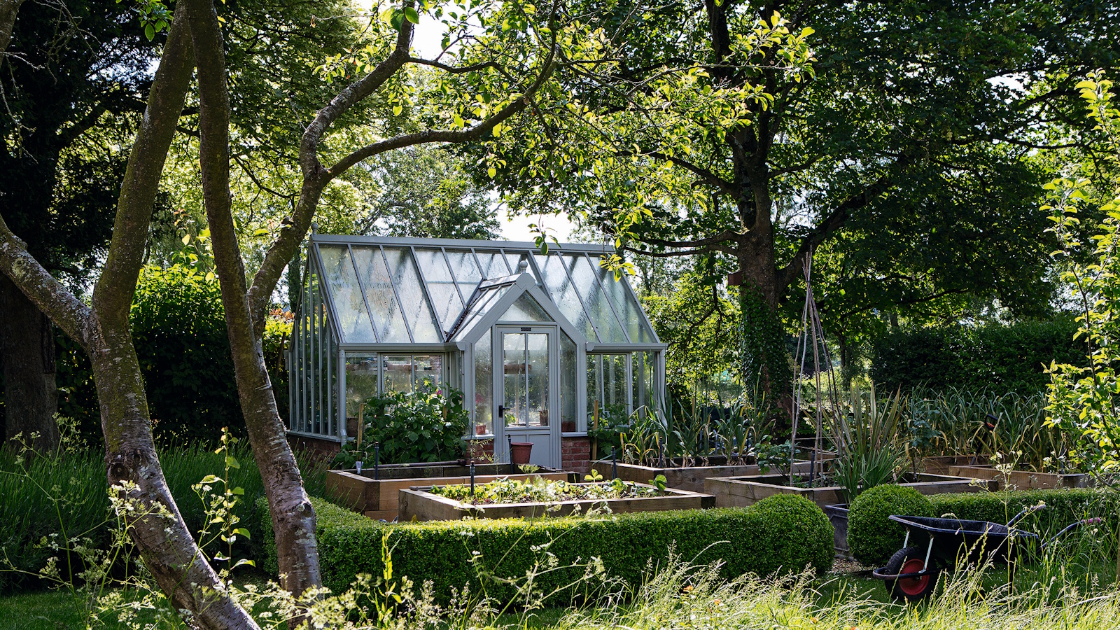 Greenhouse in a lush, green garden during summer, surrounded by established trees
